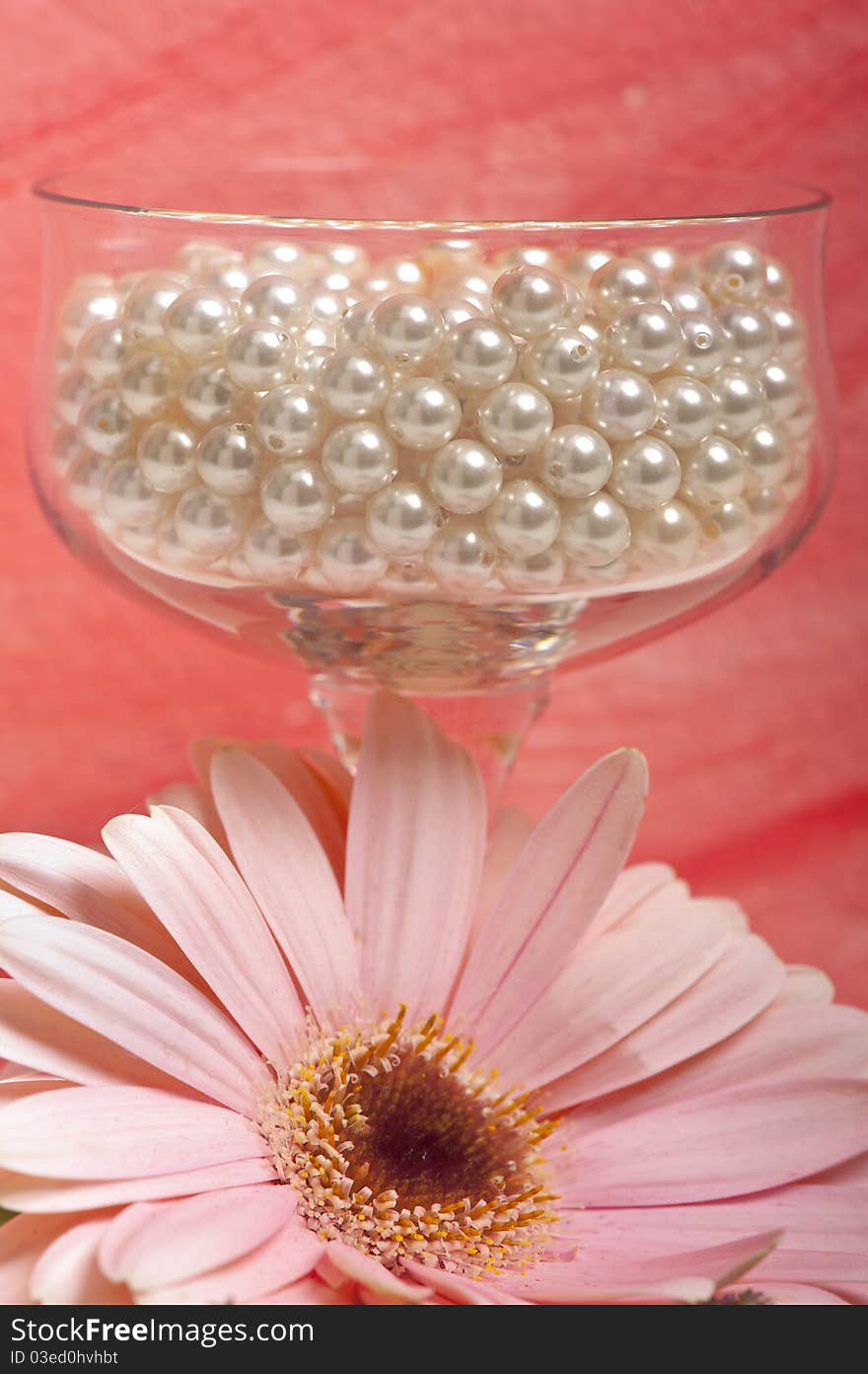 Pearls in a crystal glass, flower on pink background. Pearls in a crystal glass, flower on pink background