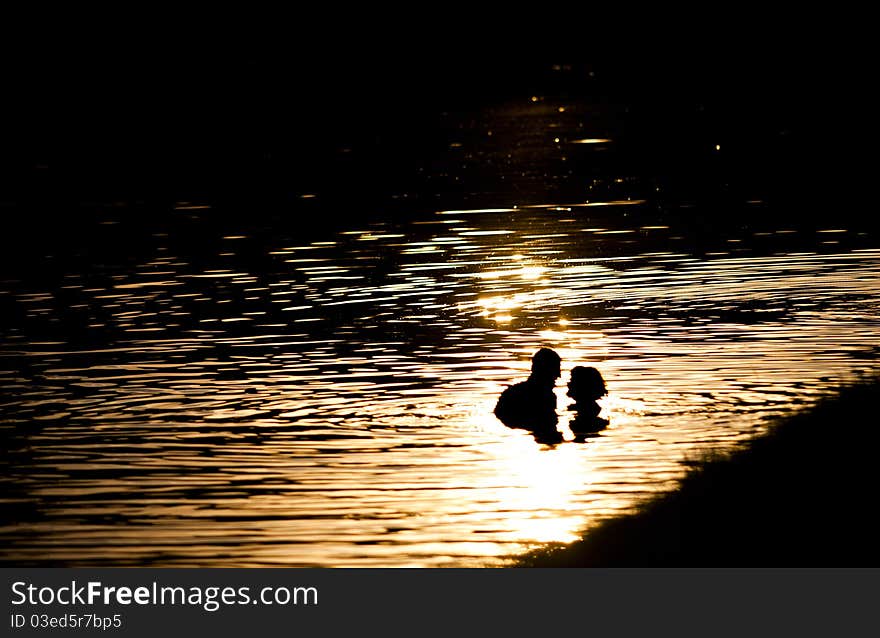 A man and a woman in love in the lake in rays of sun on sunset. A man and a woman in love in the lake in rays of sun on sunset