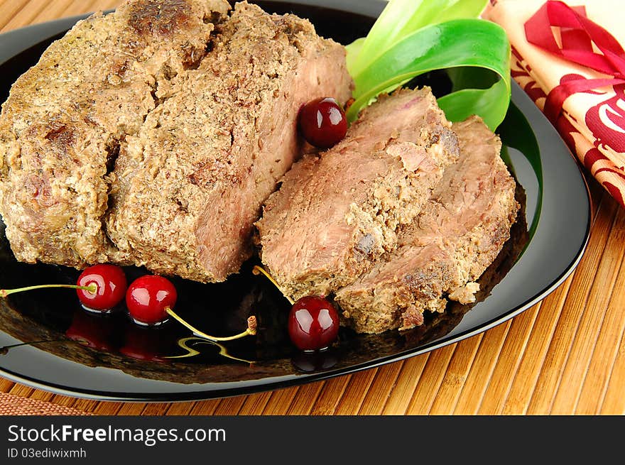 Succulent roast beef meat slices with cherry on a black plate. Succulent roast beef meat slices with cherry on a black plate