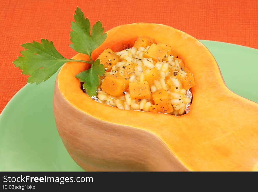 Half pumpkin filled with pumpkin risotto served on a green plate