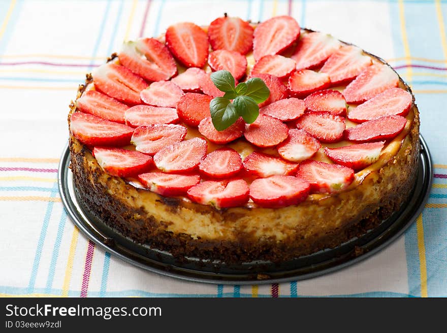 Photo of a whole good looking vanilla cheesecake topped with sliced strawberries and mint. Photo of a whole good looking vanilla cheesecake topped with sliced strawberries and mint.