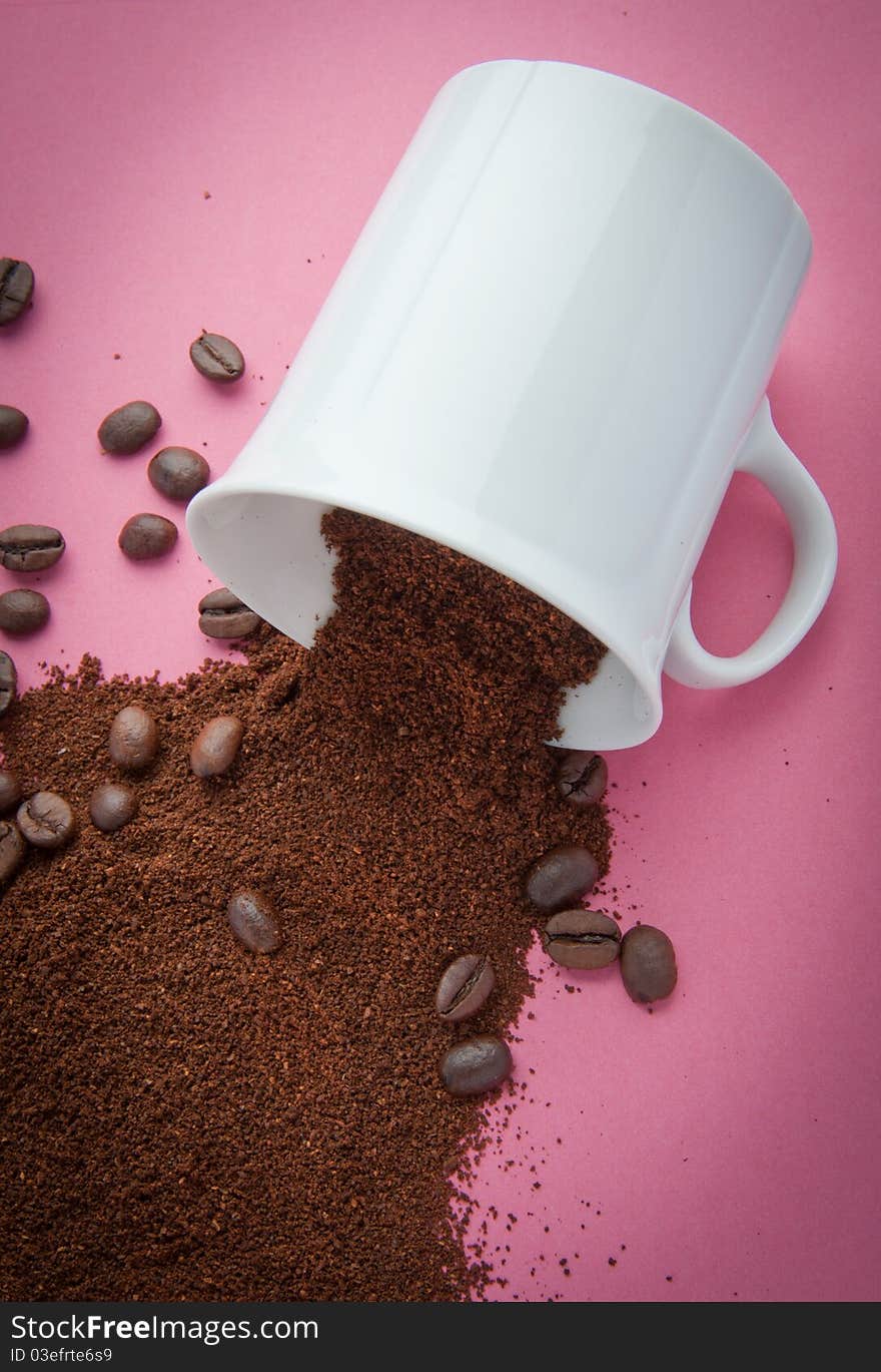 Cup with coffee grind and coffee beans spilled on a pink background. Cup with coffee grind and coffee beans spilled on a pink background