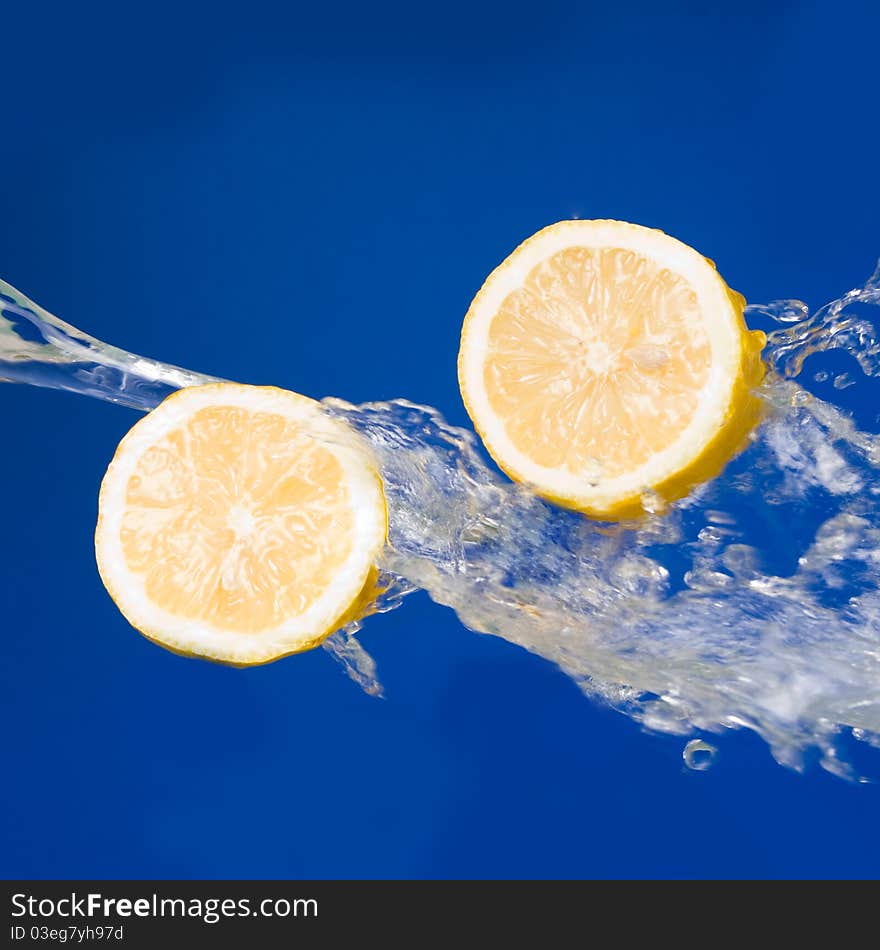 Two halves of lemon in the splashes of water on a blue background