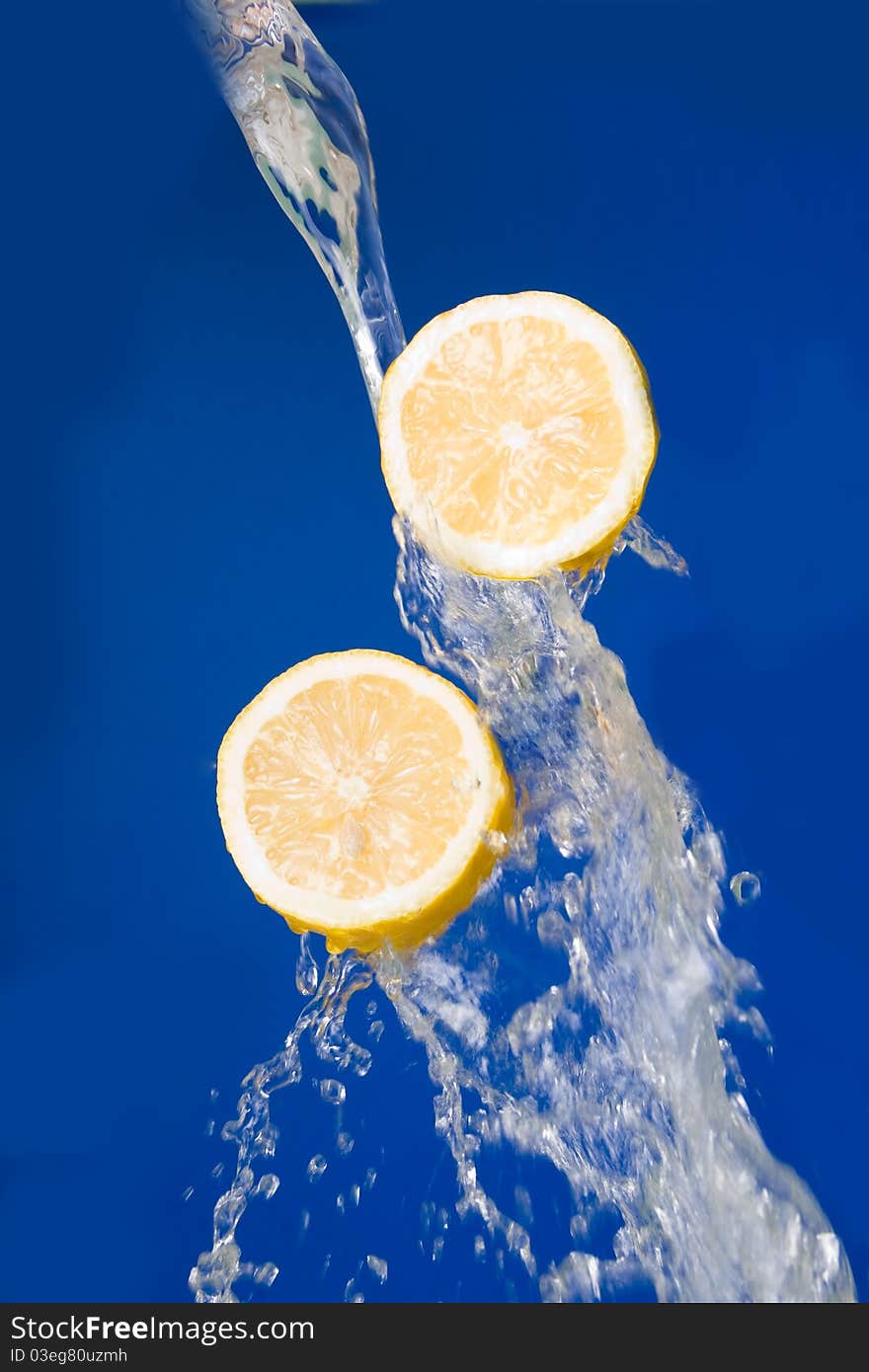 Two halves of lemon  in the splashes of water on a  blue background. Two halves of lemon  in the splashes of water on a  blue background