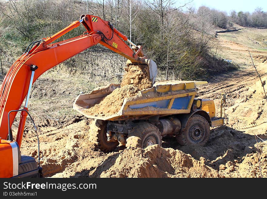 Excavator loading truck shot against the background of the pit and blue sky. Excavator loading truck shot against the background of the pit and blue sky