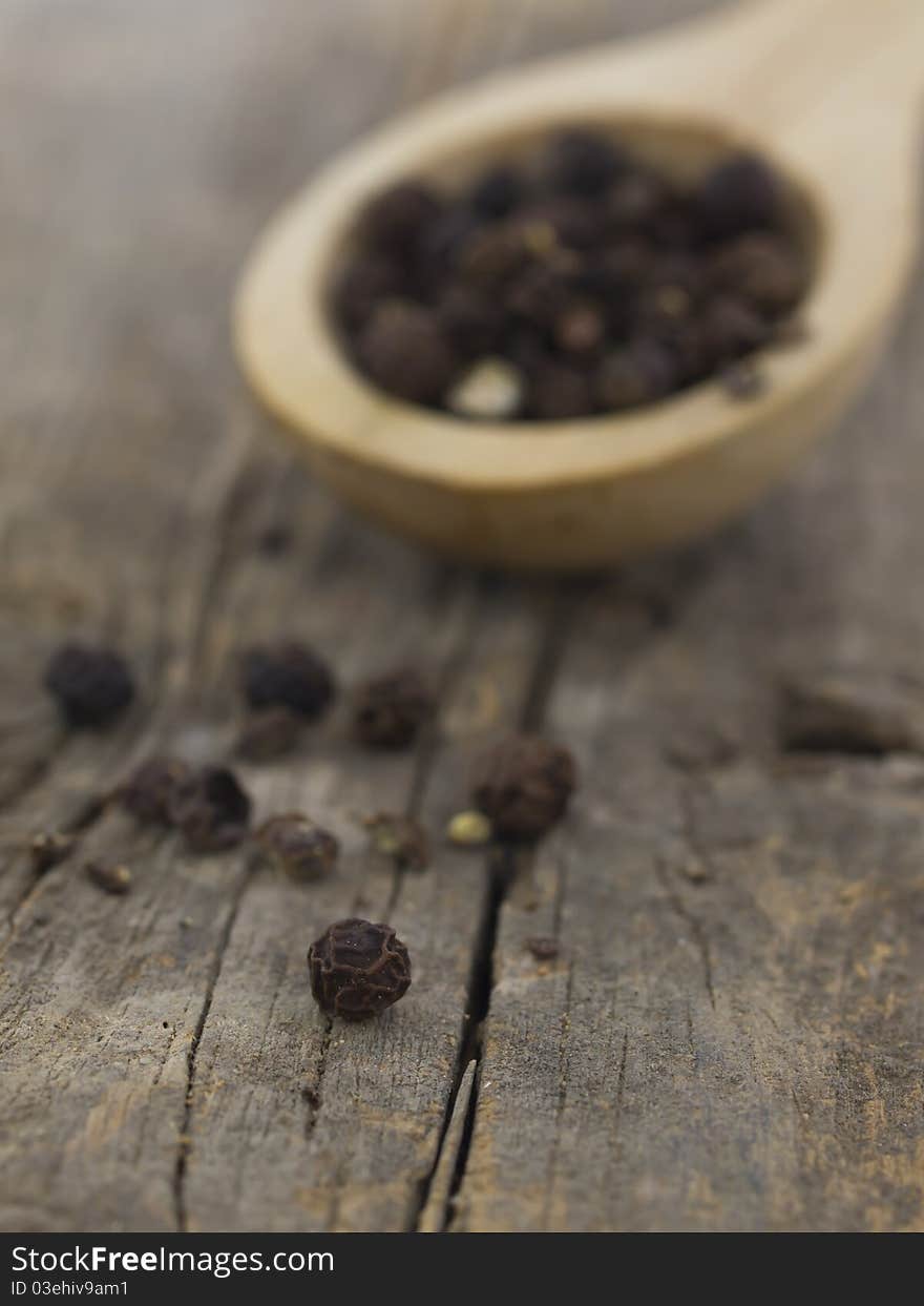 Pepper grains in the spoon on the wooden background. Pepper grains in the spoon on the wooden background