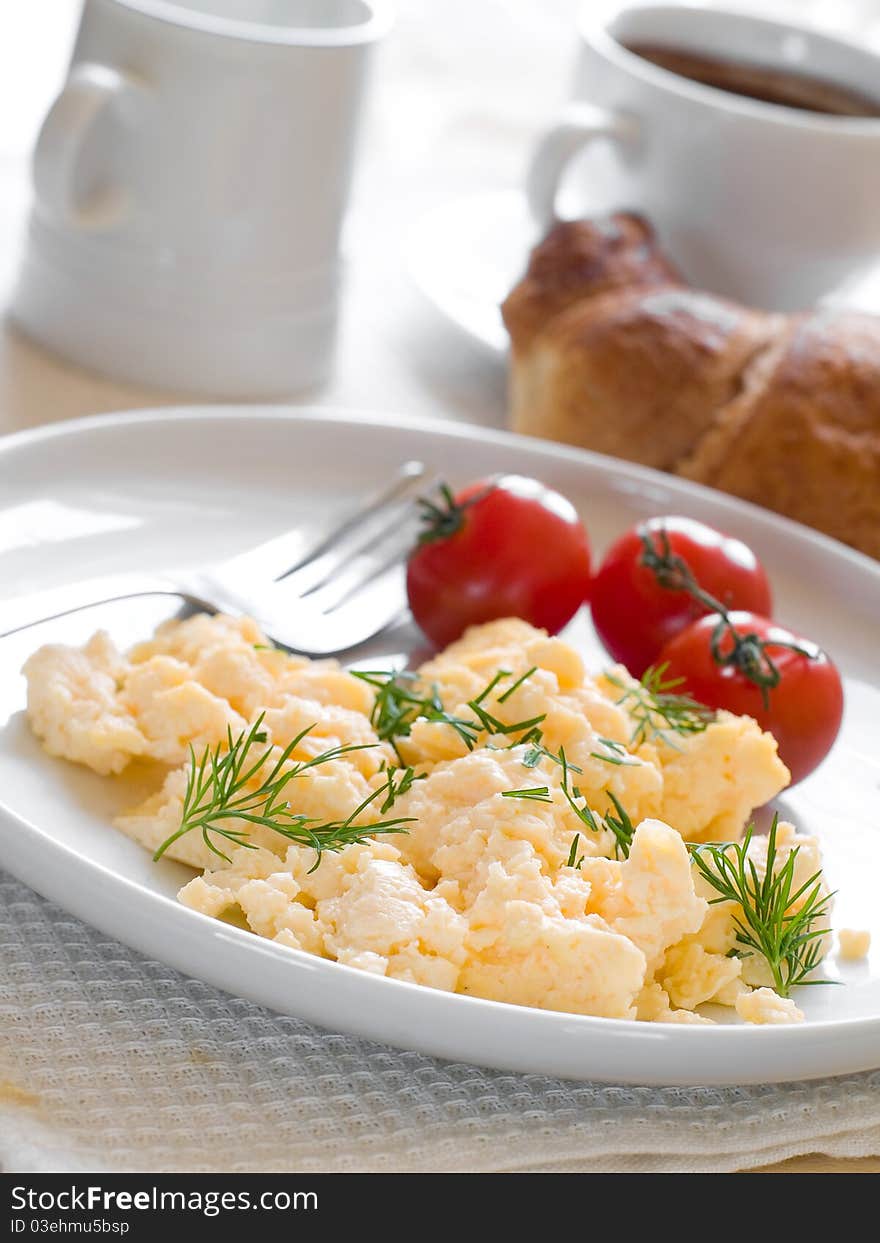 A plate of creamy scrambled eggs garnished with dill, a cup of coffee with milk. A plate of creamy scrambled eggs garnished with dill, a cup of coffee with milk