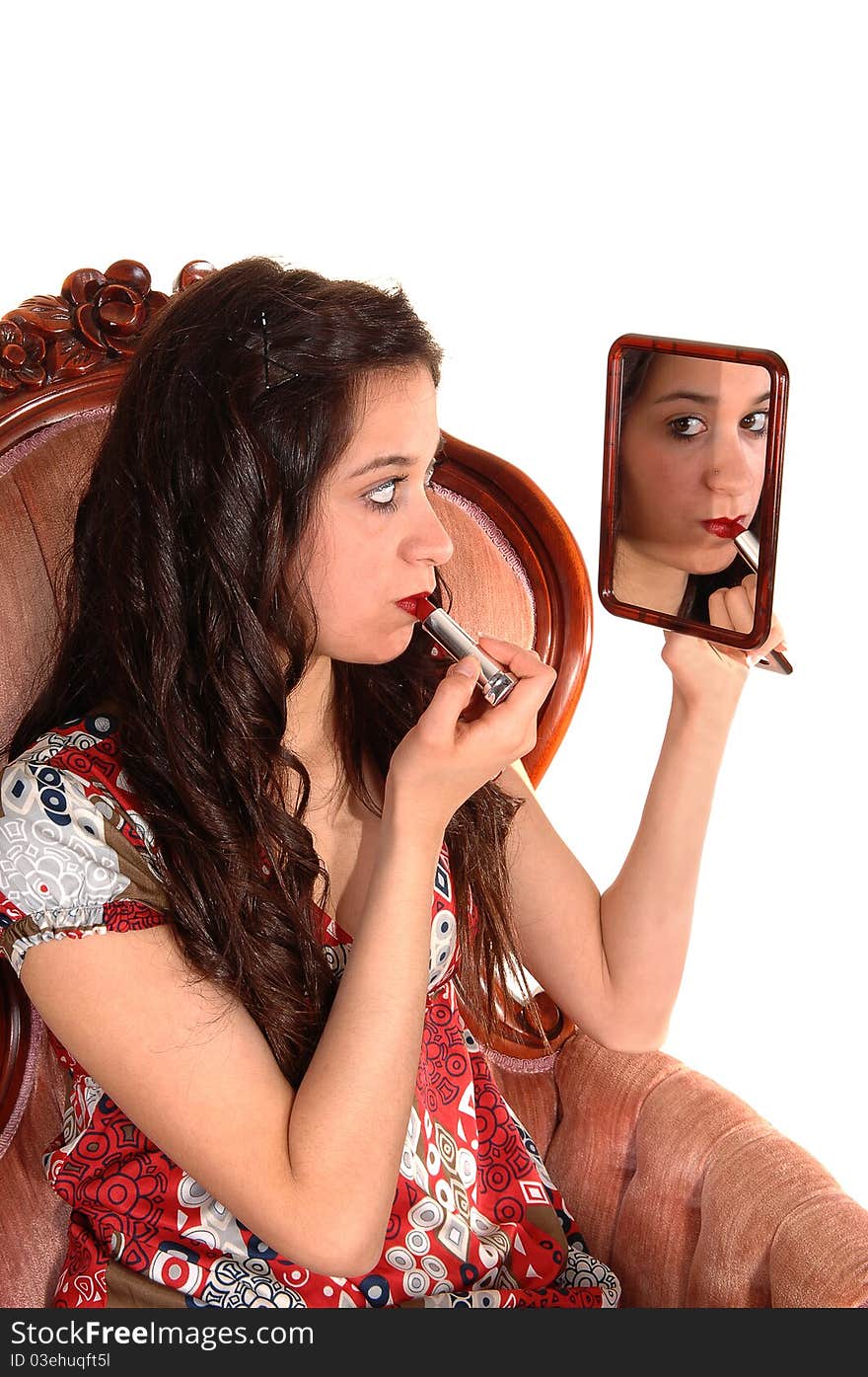 A beautiful young woman sitting in a pink armchair, holding a mirror
and putting red lipstick on, over white background. A beautiful young woman sitting in a pink armchair, holding a mirror
and putting red lipstick on, over white background.