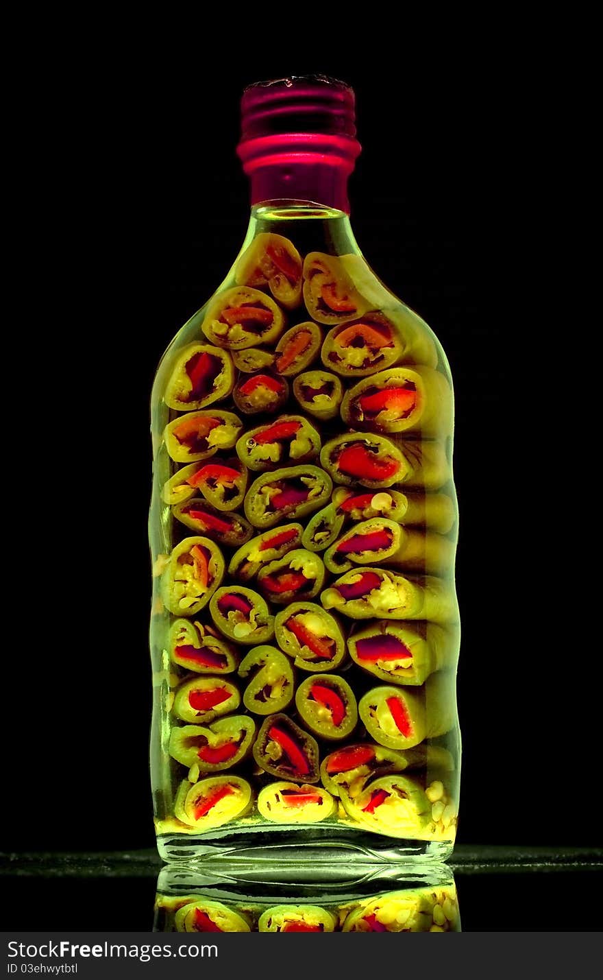 High vitality image of a bottle of sliced green peppers against a black background. High vitality image of a bottle of sliced green peppers against a black background