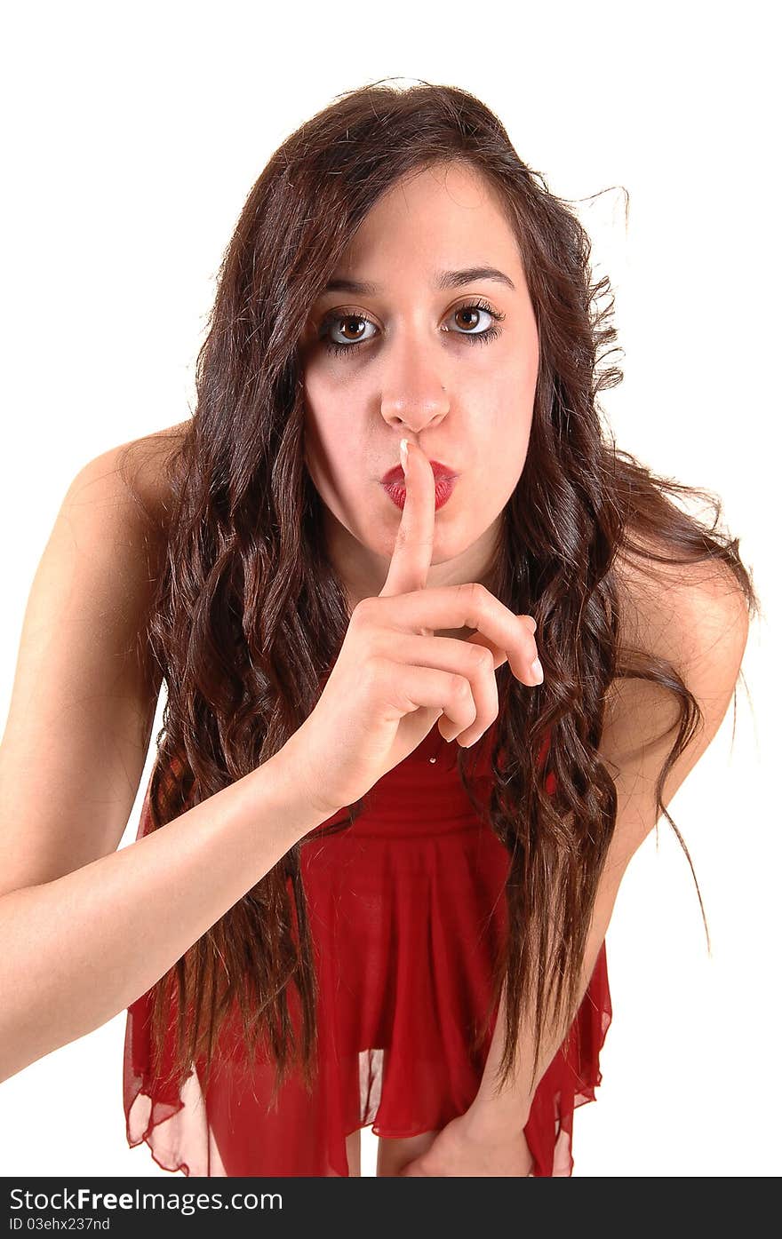 A young pretty woman in a red dress sign, be quiet, to the photographer with her long brunette curly hair, on white background. A young pretty woman in a red dress sign, be quiet, to the photographer with her long brunette curly hair, on white background.