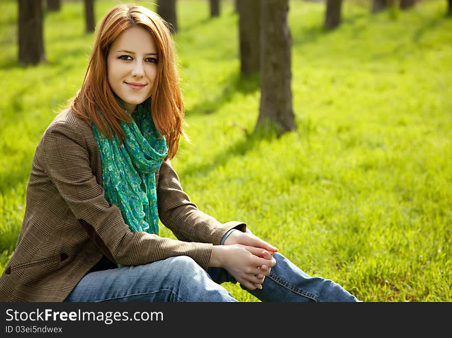 Beautiful red-haired girl sitting at green grass at park. Beautiful red-haired girl sitting at green grass at park.