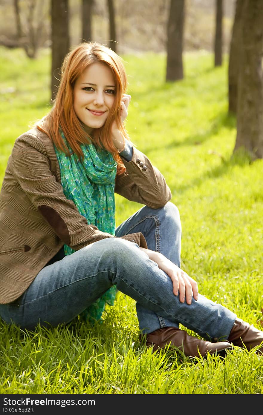 Beautiful red-haired girl sitting at green grass at park. Beautiful red-haired girl sitting at green grass at park.