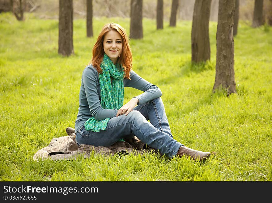 Beautiful red-haired girl sitting at green grass at park. Beautiful red-haired girl sitting at green grass at park.