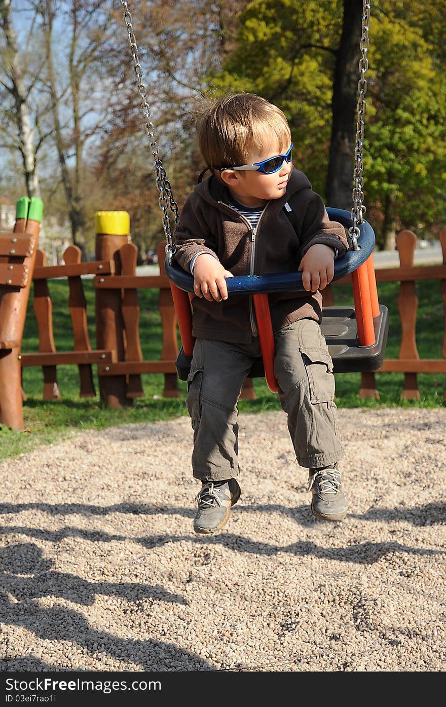 Young boy with sunglasses sitting on a swing and having fun on a playground. Young boy with sunglasses sitting on a swing and having fun on a playground