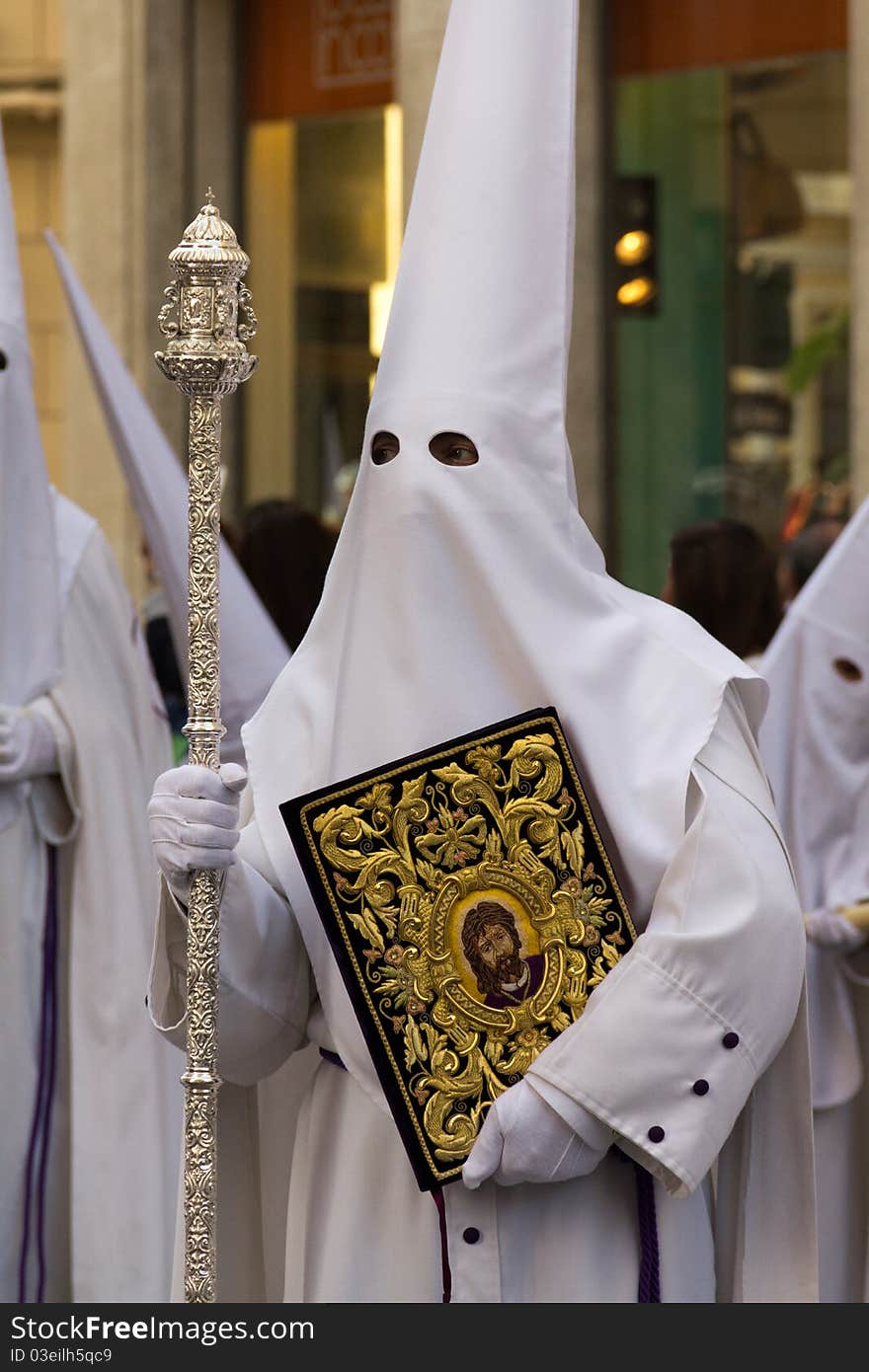 Man with white hood holding a silver staff and a golden scapular. Man with white hood holding a silver staff and a golden scapular