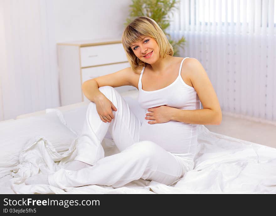 Young pregnant woman sitting on bed. Young pregnant woman sitting on bed