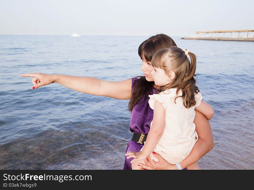 Mom hugs her daughter and shows on the sea. Mom hugs her daughter and shows on the sea