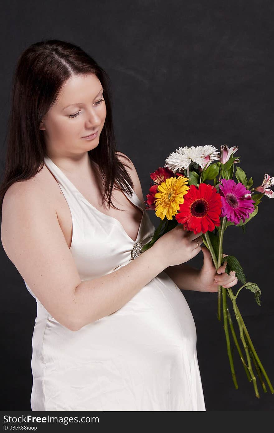 Pregnant woman in a white dress looking at a bouquet gerbera