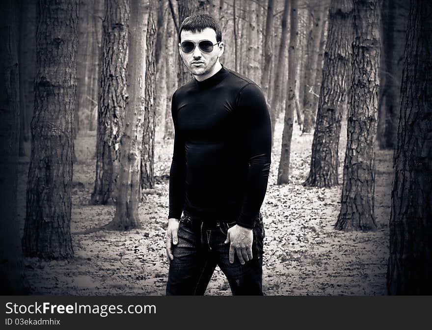 Young man in black clothes and sunglasses at forest