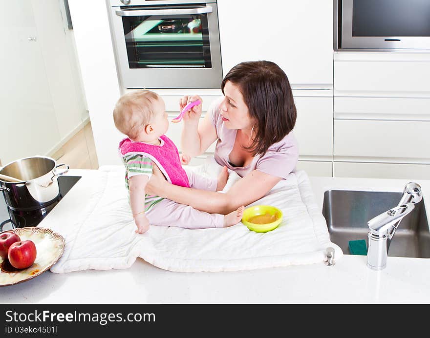 Young mother is feeding her baby in a modern kitchen setting. Young mother is feeding her baby in a modern kitchen setting.