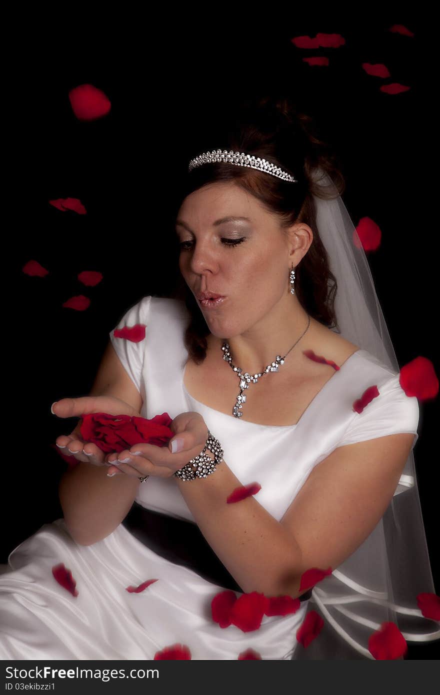 A bride holding rose petals in her hands blowing on them as they fly over her head. A bride holding rose petals in her hands blowing on them as they fly over her head.