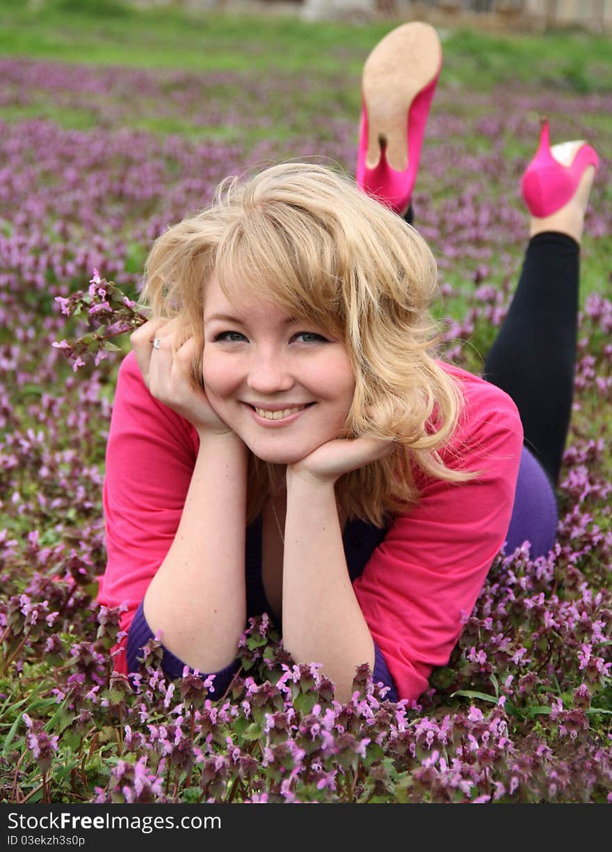 Young beautiful blond cheerful woman laying on blooming field in spring. Young beautiful blond cheerful woman laying on blooming field in spring