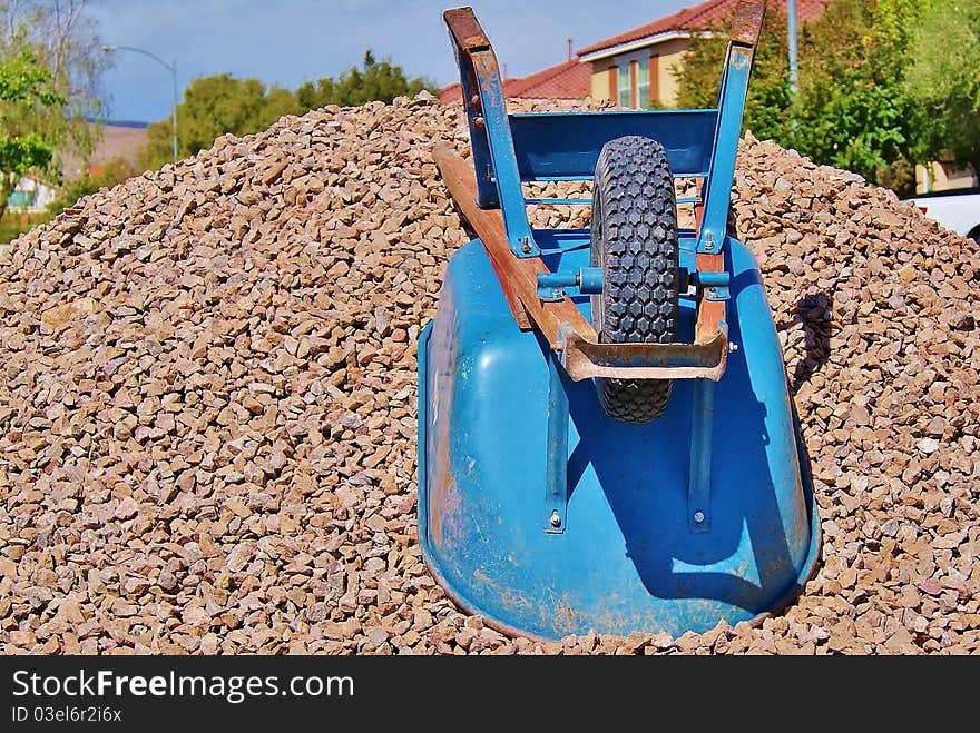 Wheelbarrow on Gravel Pile in Front of Houses