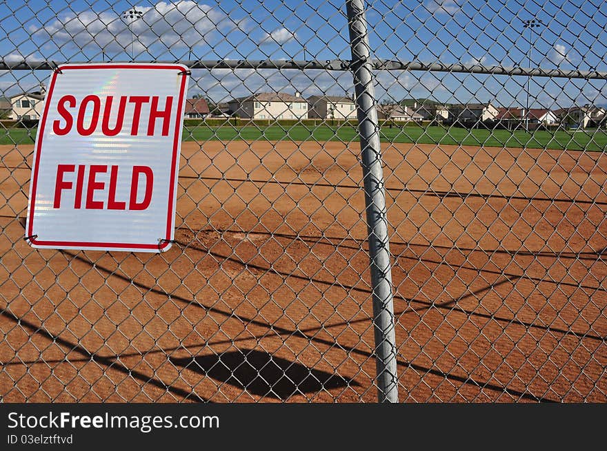 A view of a softball field from behind home plate, looking through the back stop.