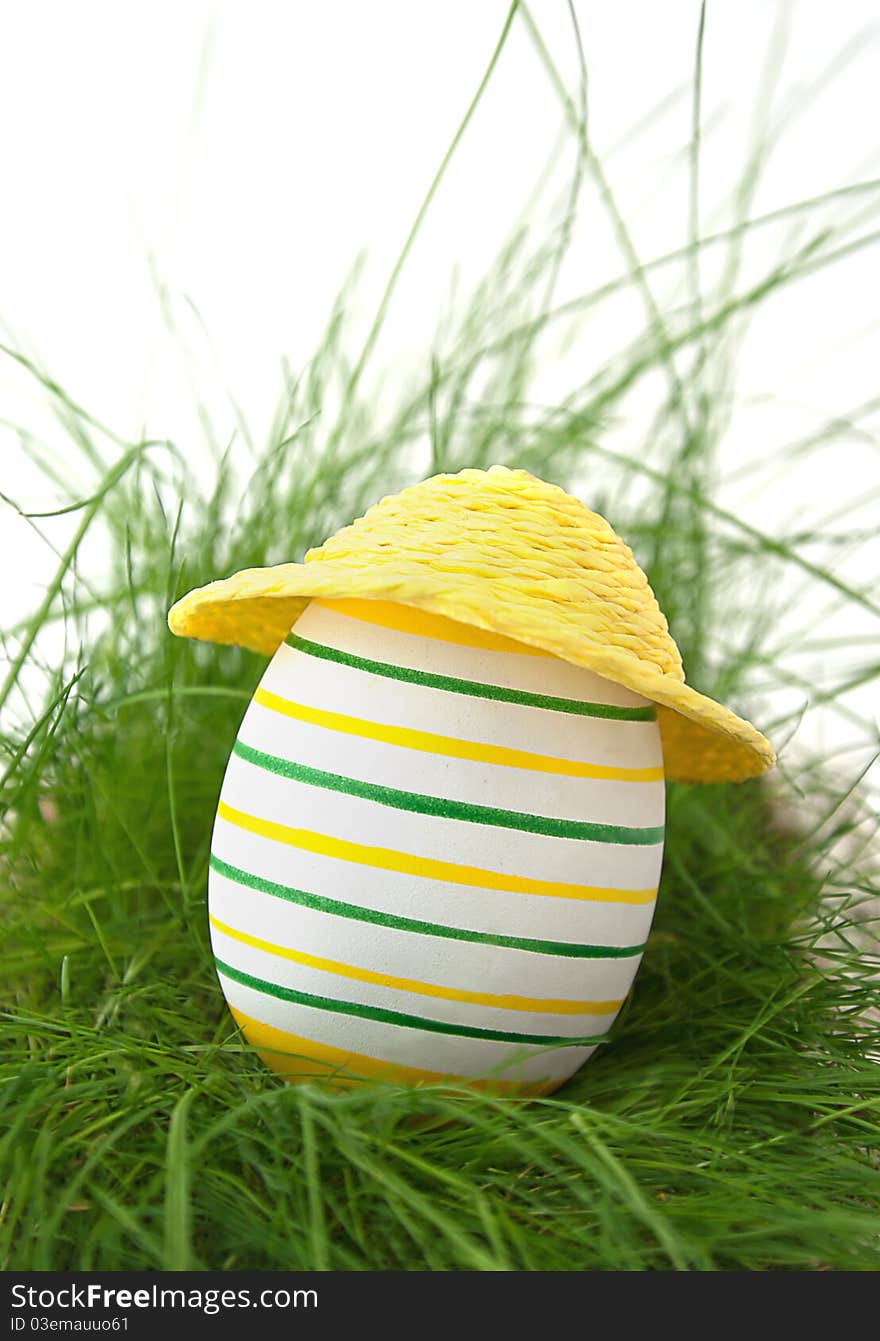 Easter egg in straw yellow hat in green grass