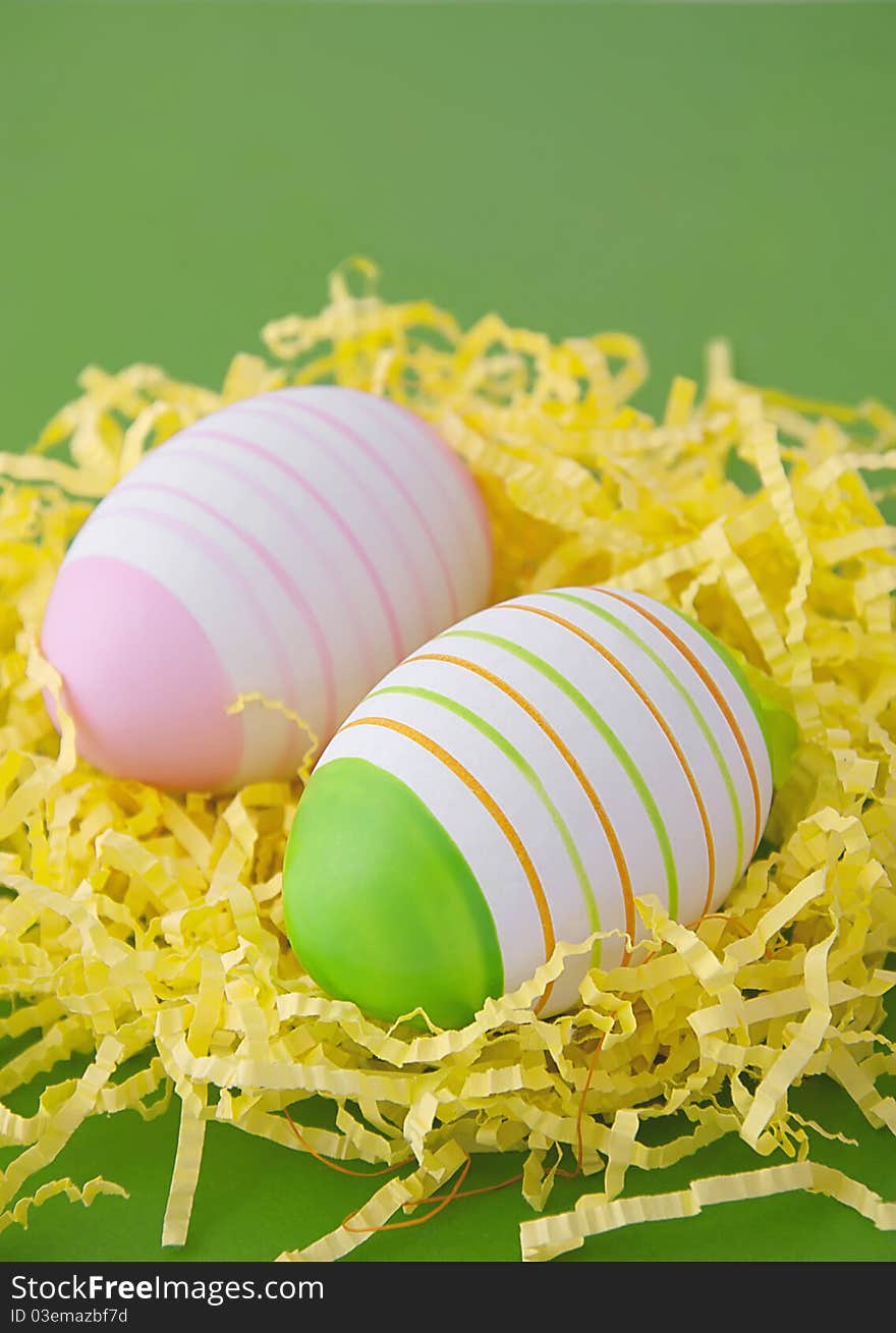 Two easter eggs in yellow nest on green background