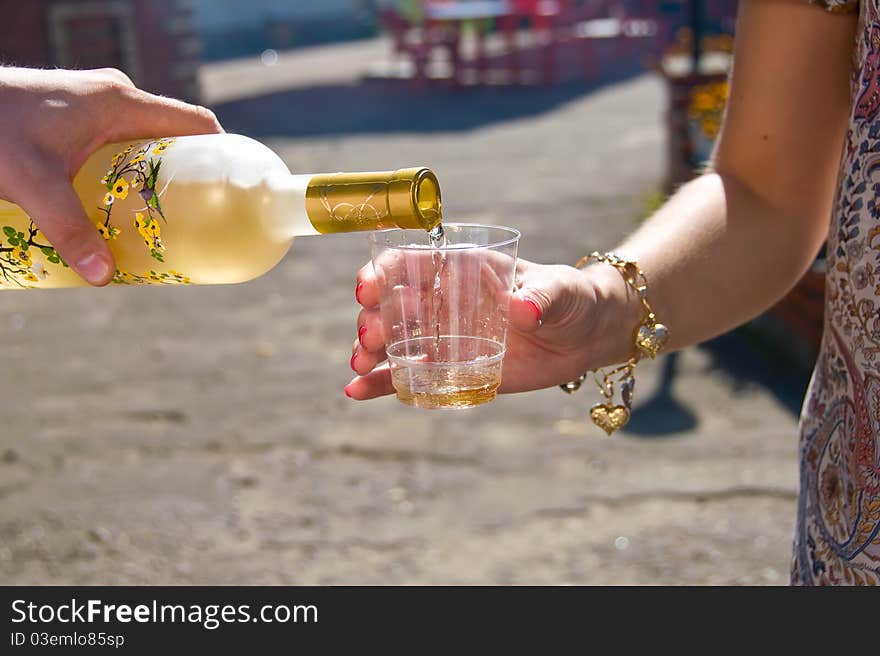 From the sun-lit bottles of hand pours wine into a glass. From the sun-lit bottles of hand pours wine into a glass