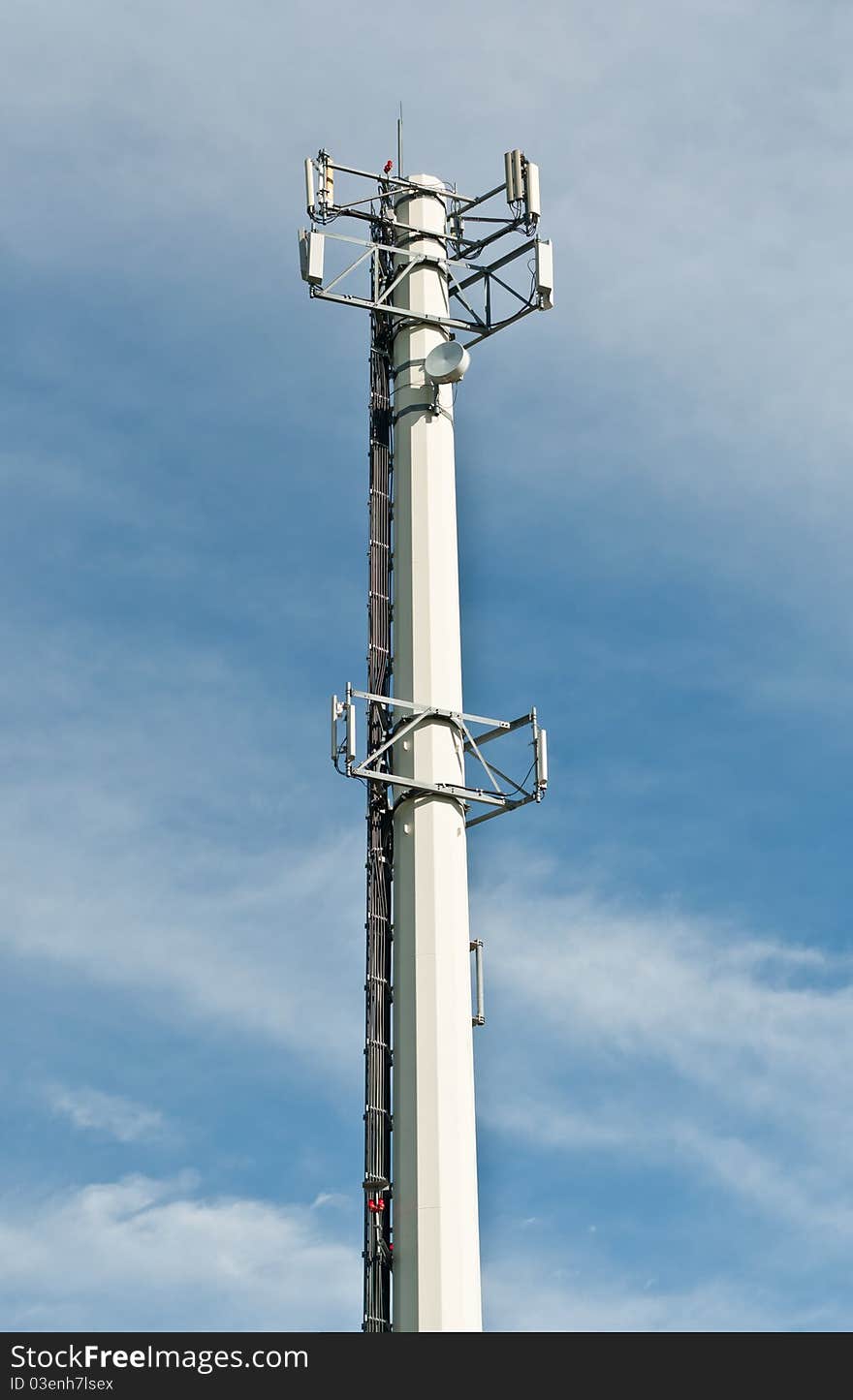 A telecom antenna tower stands out against a blue sky with white clouds.