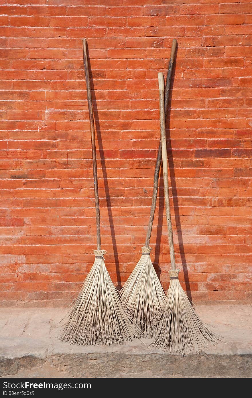 Three brooms against a red wall