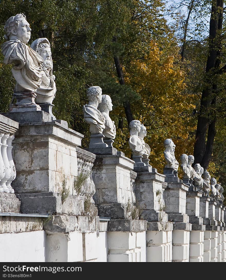 Old white wall with antique statues against a background of autumnal trees