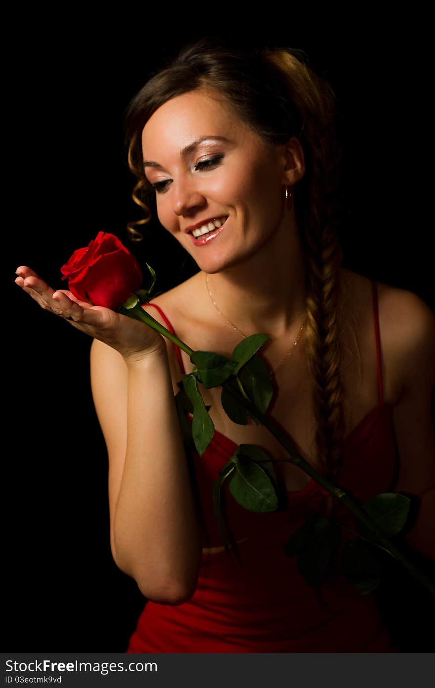 Smiling girl looking at a red rose on a black background. Smiling girl looking at a red rose on a black background