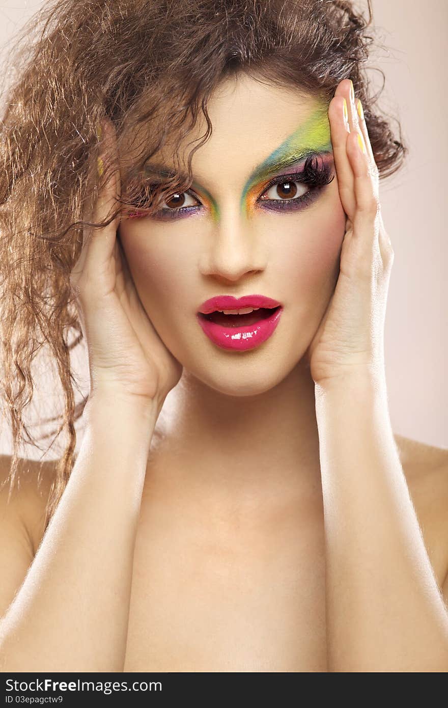 Beautiful young attracive female face with bright fashion multicolored make-up and beauty yellow manicure of fingernails