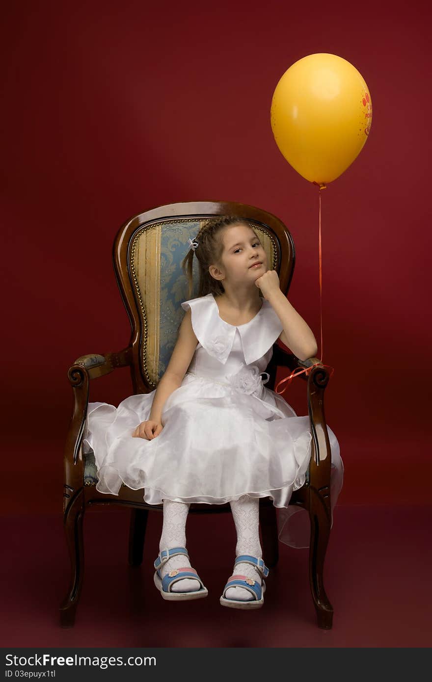 Studio portrait of a young pretty girl sitting on the armchair and with yellow balloon. Studio portrait of a young pretty girl sitting on the armchair and with yellow balloon