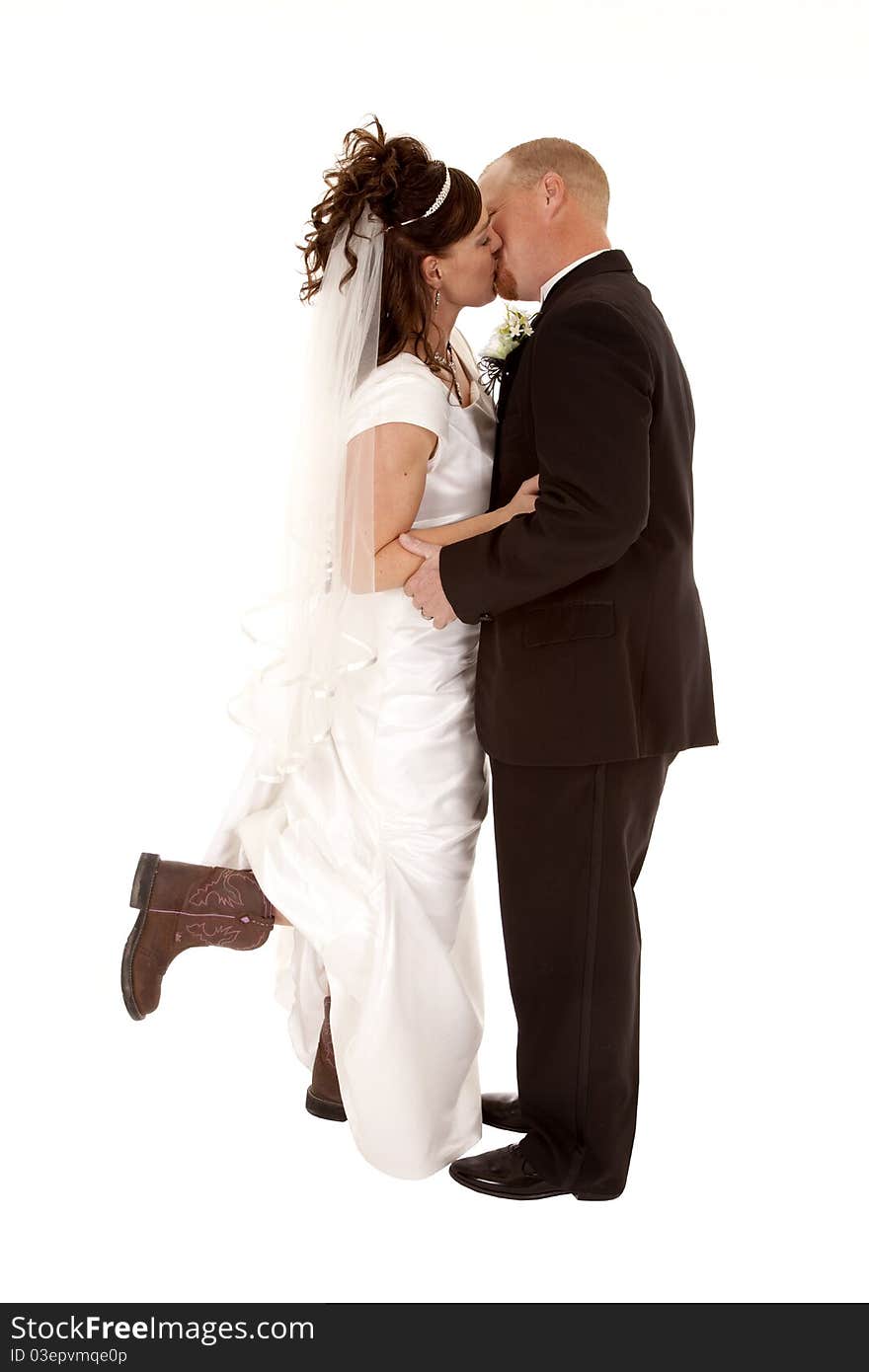 A bride and groom kissing and holding each other.  The bride is holding her foot up with a cowboy boot on. A bride and groom kissing and holding each other.  The bride is holding her foot up with a cowboy boot on.