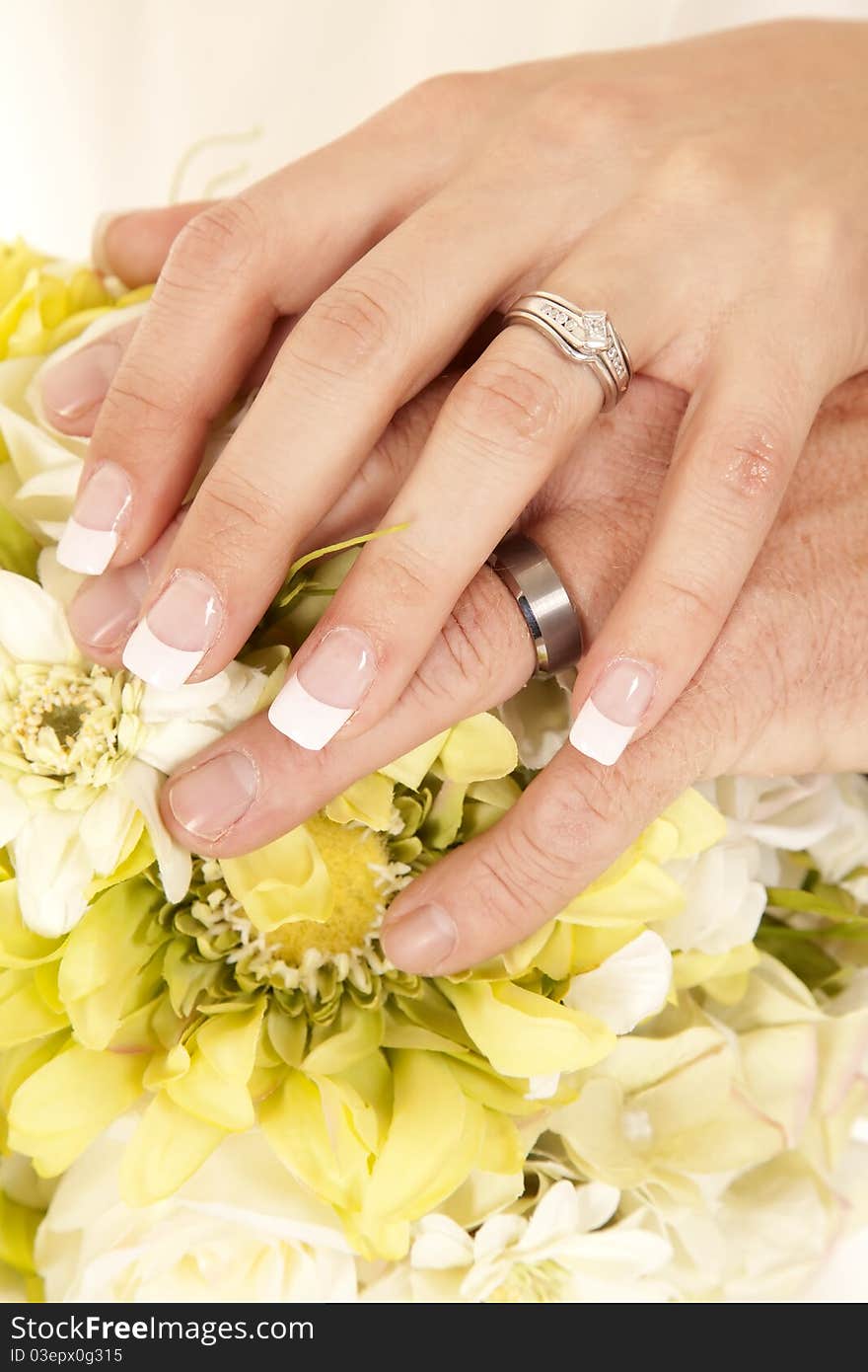 A bride and goom with their hands on top of the flowers, showing off their rings. A bride and goom with their hands on top of the flowers, showing off their rings.