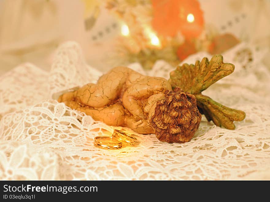 Gold wedding bands on white lace next to an angle. Gold wedding bands on white lace next to an angle