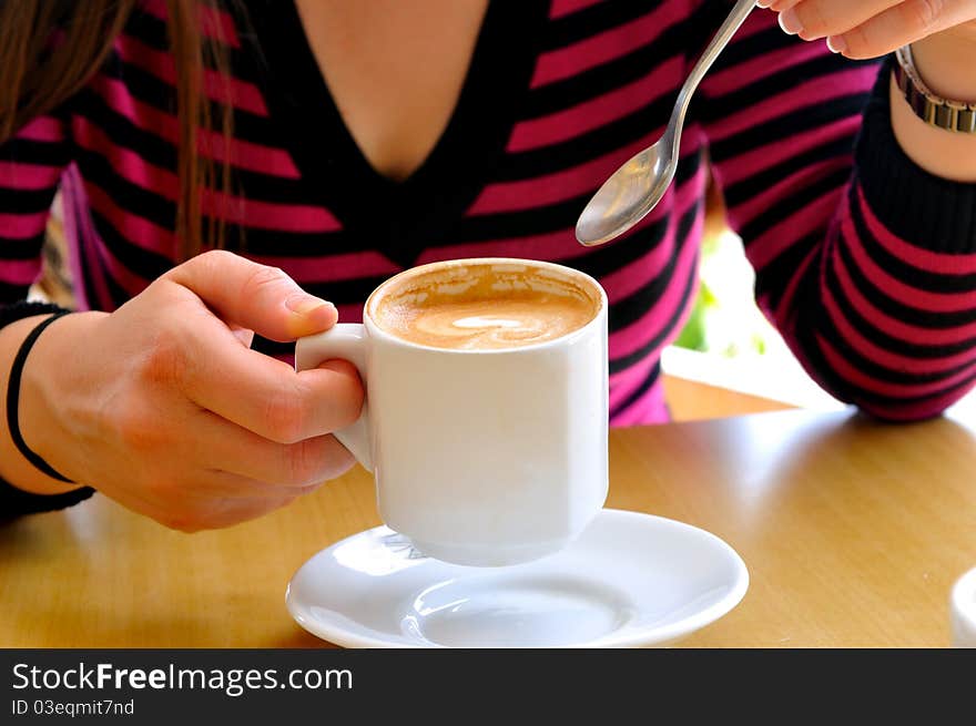 Females holding a cup of cappuccino and a spoon in the other hand. Females holding a cup of cappuccino and a spoon in the other hand