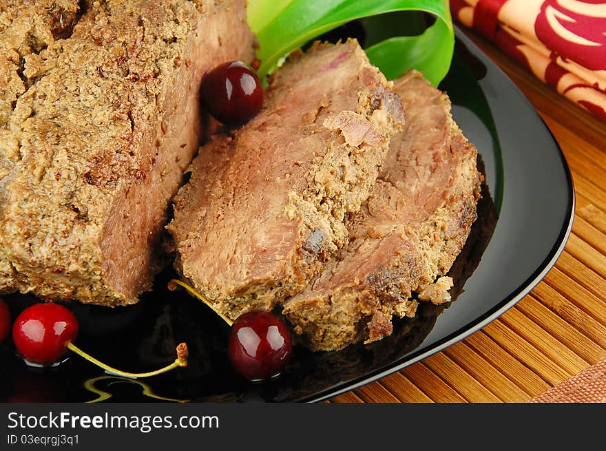 Succulent roast beef meat slices with cherry and leek on a black plate. Succulent roast beef meat slices with cherry and leek on a black plate