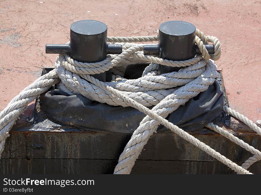 Old ropes around rusty mooring bollard in a dock