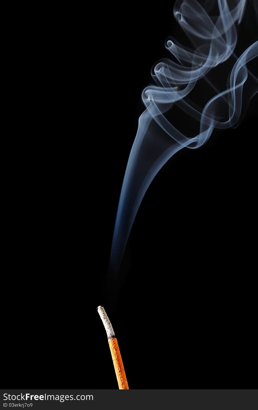 A burning incense stick with white smoke on a black background. A burning incense stick with white smoke on a black background