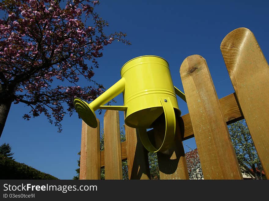 Yellow watering can put-on a wooden fence