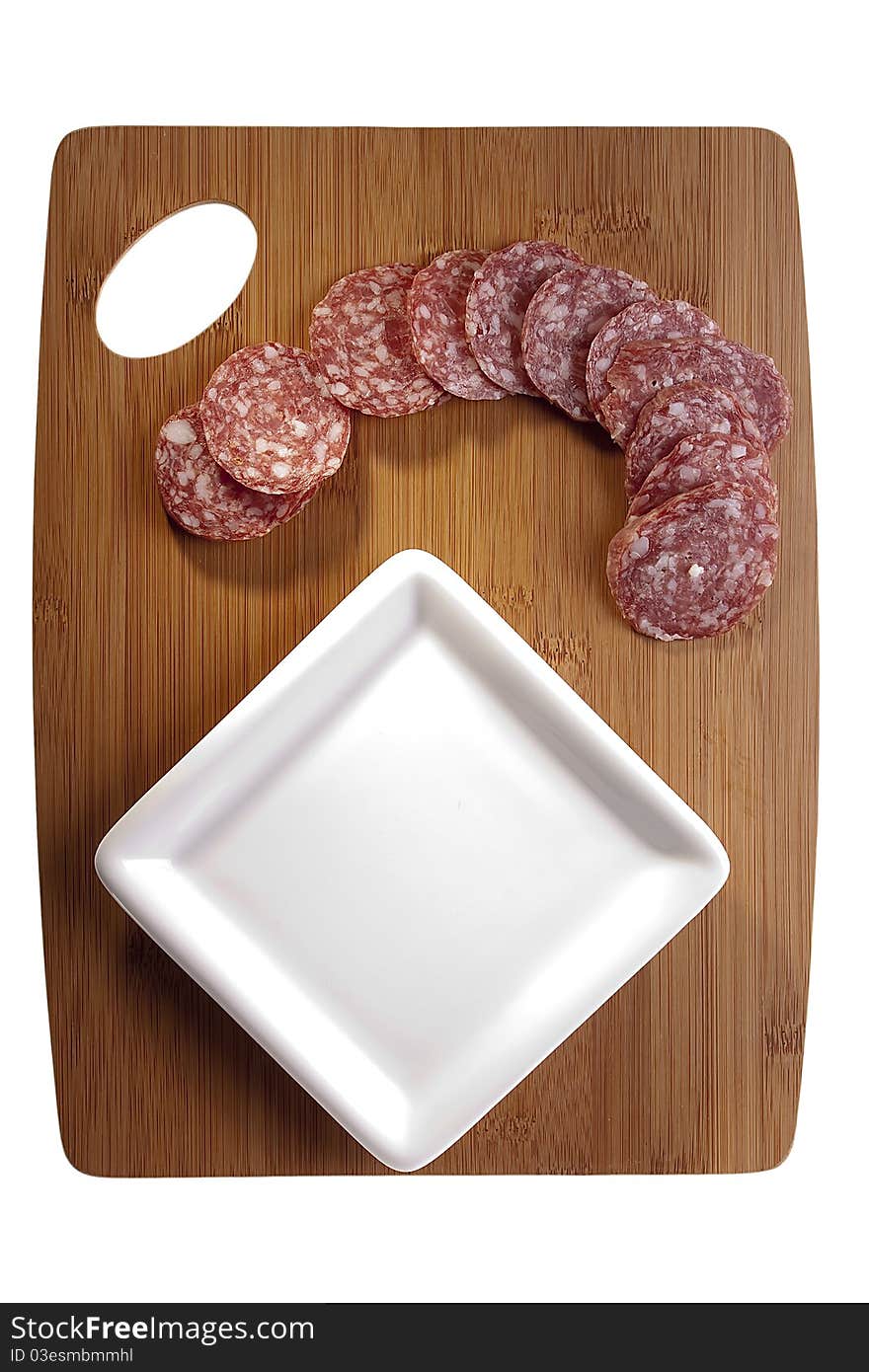 Sliced salami laying next to a white plate on a cutting board.