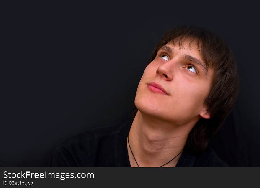 A young guy looks up dreaming on a dark background