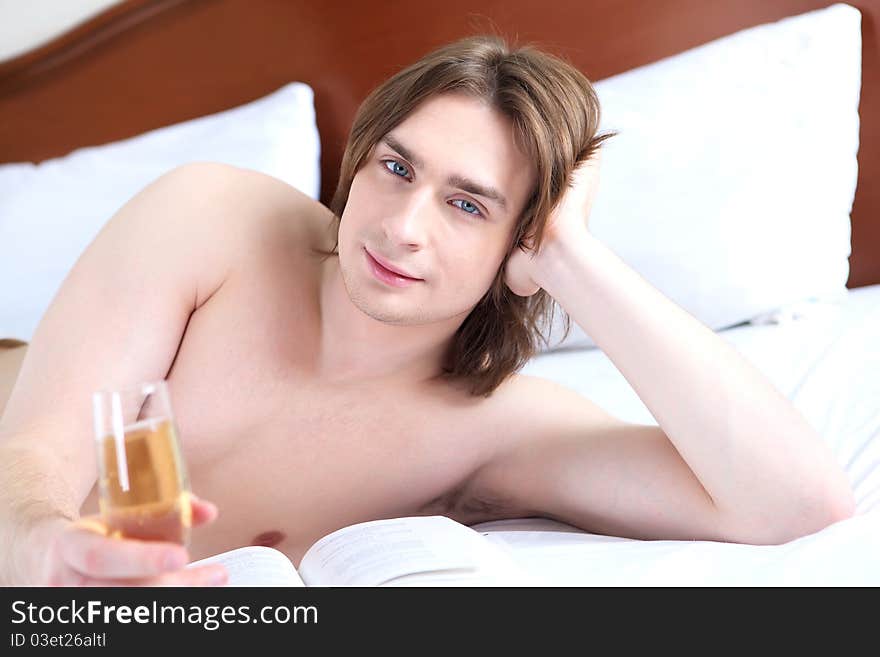 Portrait of a young man in bed with a glass of campagne