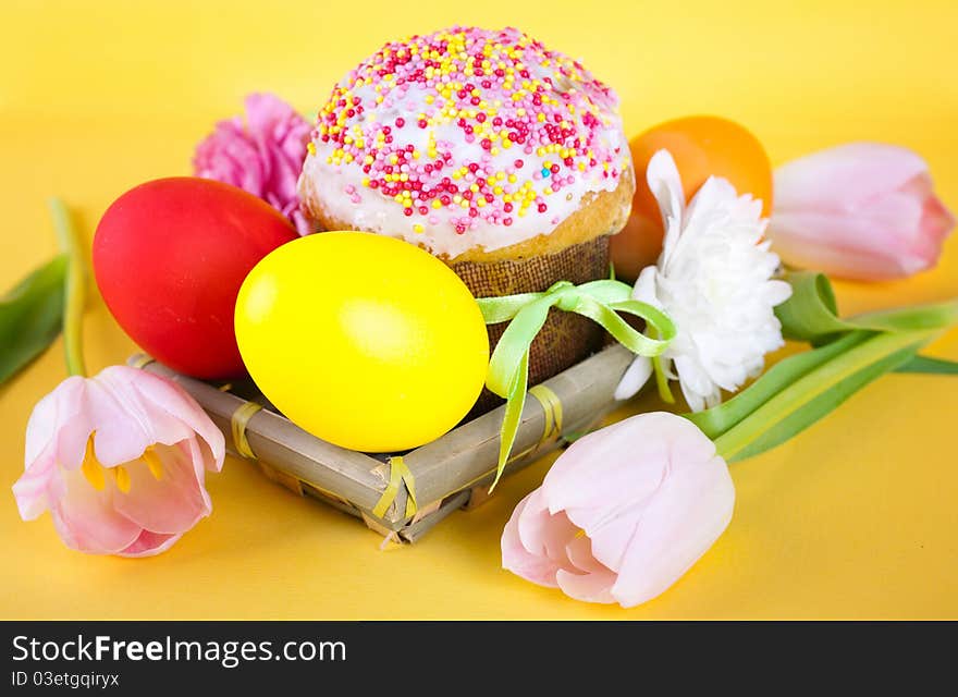 Easter cake, coloured easter eggs and spring flowers on a yellow background