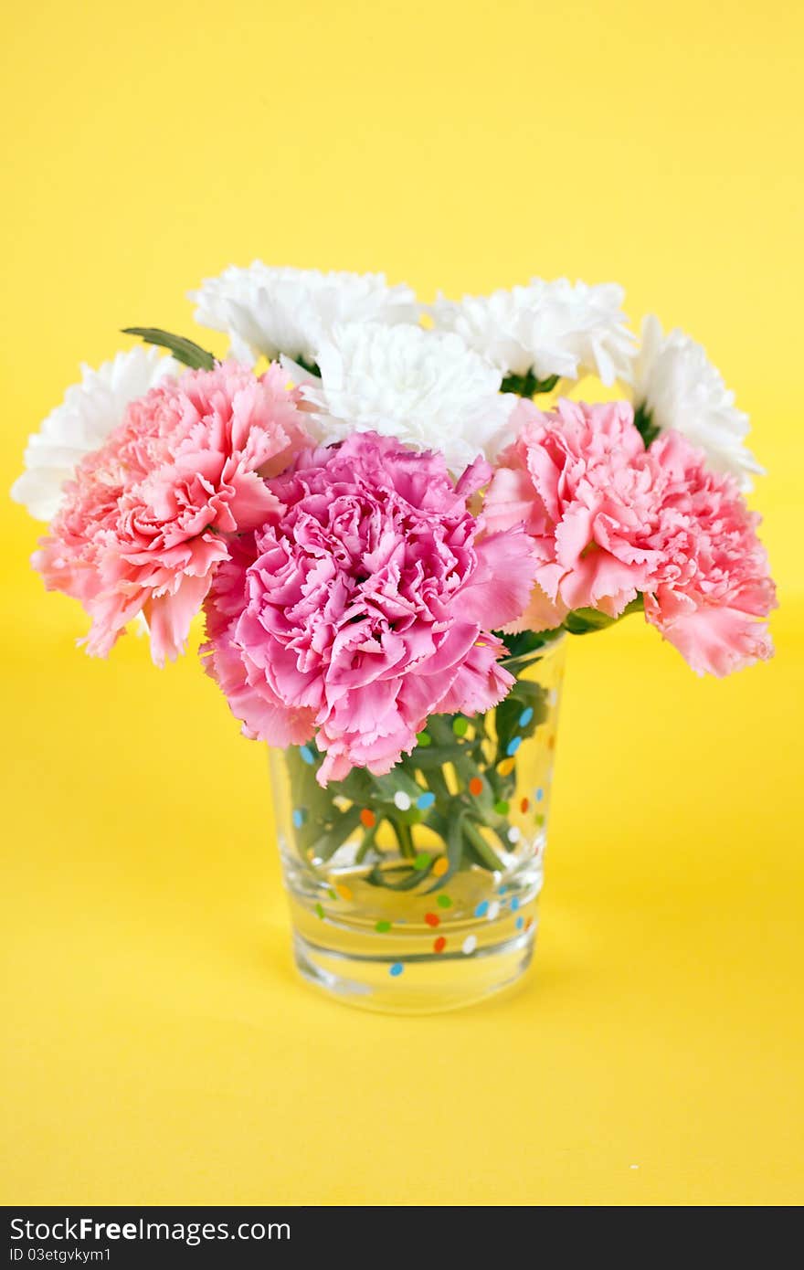 Bunch of flowers: white chrysanthemum and pink carnations (Dianthus caryophyllus‎) in a vase on yellow background